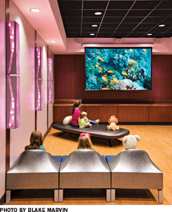 Children sit in a colorful theater room and watch a movie.
