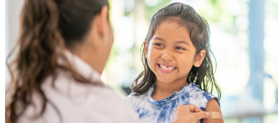 A girl smiles as a doctor applies a bandage after a vaccine. 