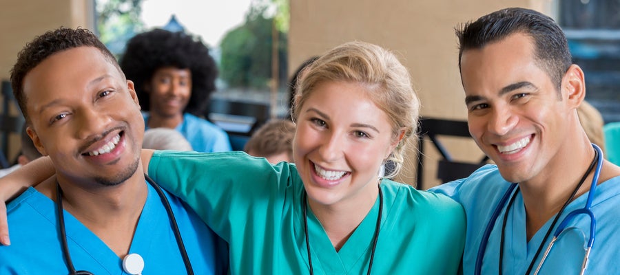 A smiling woman in scrubs stands between two men smiling in scrubs. 
