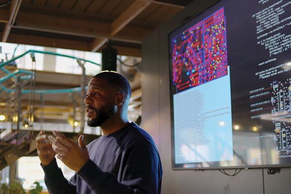 Man presenting in front of large computer screen
