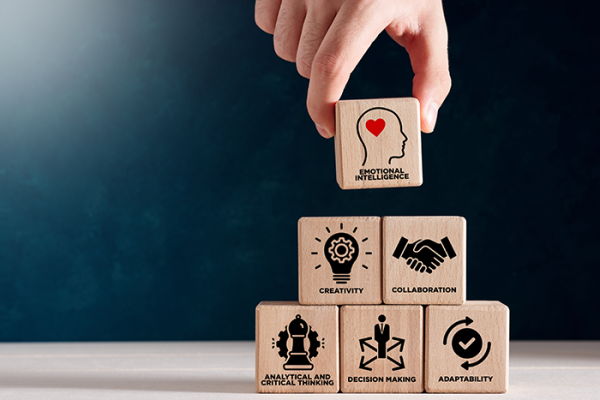 Person stacking blocks with words and images printed on them "emotional intelligence" "collaboration" etc. 