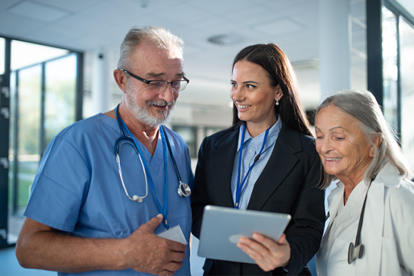 Doctor and nurse look at a tablet held by woman in a suit