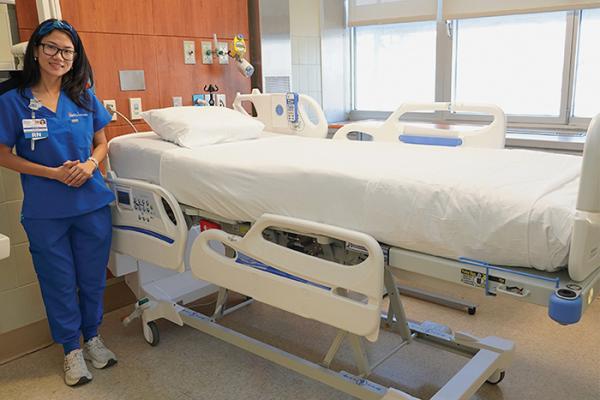Nurse Mandie Xie at NYC Health + Hospitals/Harlem stands next to Hillrom Centralla smart bed