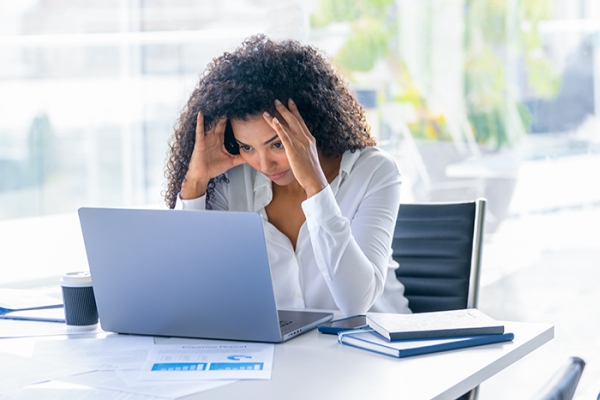 woman sitting at desk looking at laptop with hands cradling head, signaling stress