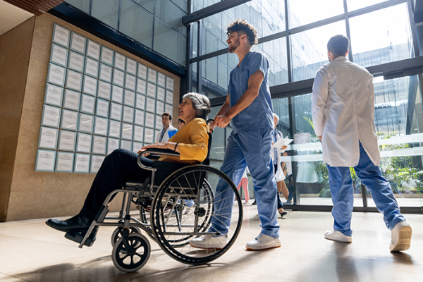 Clinician pushing patent in wheelchair across hospital lobby