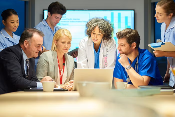 Medical and administration professionals sitting around conference table looking at laptop