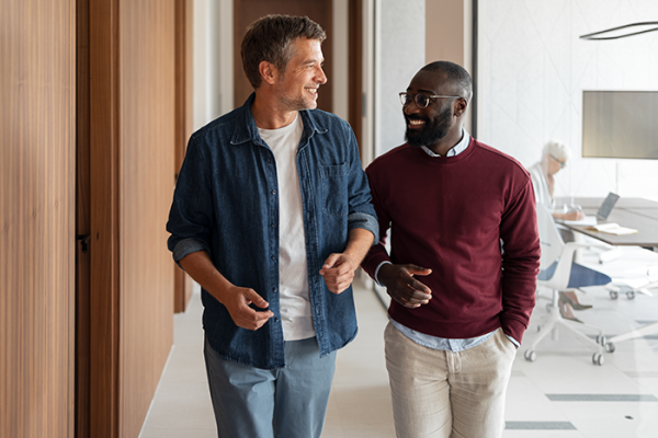 Two coworkers walking down hallway smiling and chatting 