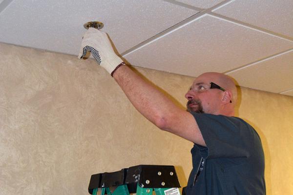 Man changing sprinkler in hallway