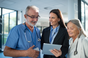 Doctor and nurse look at a tablet held by woman in a suit
