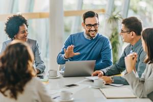 Five coworkers huddled around table in meeting room and smiling