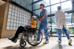 Clinician pushing patent in wheelchair across hospital lobby