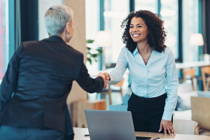 Two woman professionals shaking hands across desk
